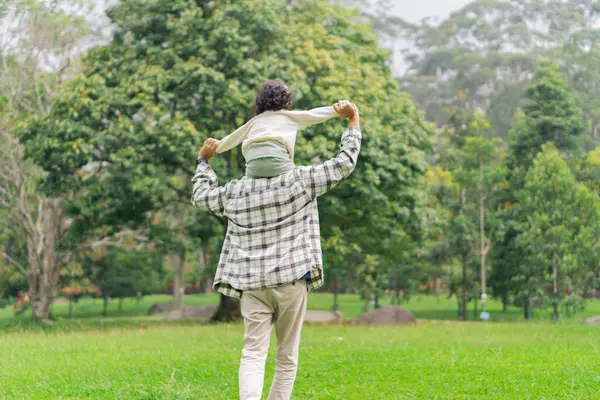 Baba ve kızının park bahçesinde sırt sırta koşarkenki görüntüsü.
