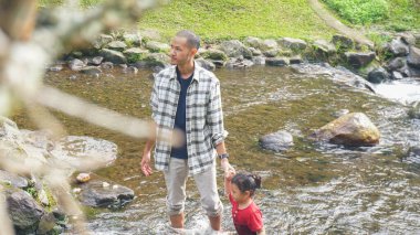 Baba ve kızı nehirde el ele oynuyorlar.