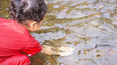 Kırmızı elbiseli bir kız çocuğu nehirde oynuyor.
