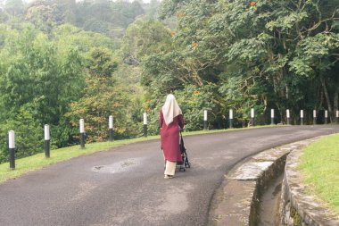 Jilbab annesi çocuğuyla parkta tek başına yürüyor.
