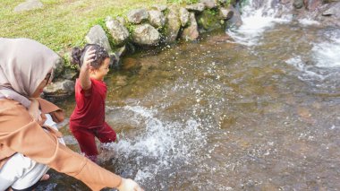 Kırmızı elbiseli bir kız çocuğu nehirde oynuyor.