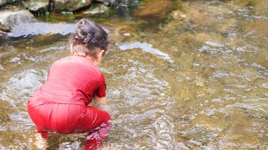 Kırmızı elbiseli bir kız çocuğu nehirde oynuyor.