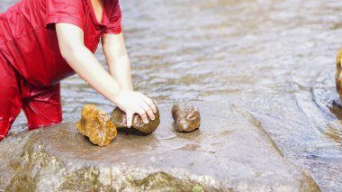 Kırmızı elbiseli, taşlı bir nehirde oynayan bir kız.