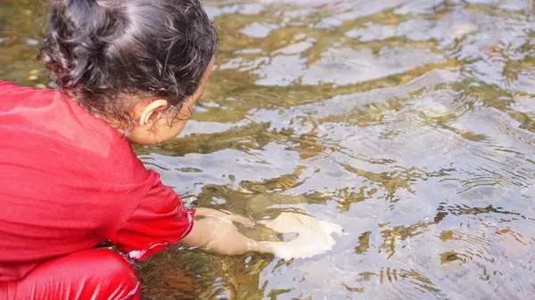 Kırmızı elbiseli bir kız çocuğu nehirde oynuyor.