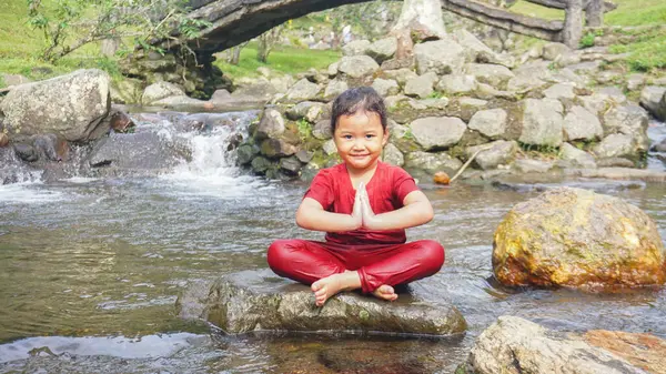 Kırmızı elbiseli bir kız çocuğu nehirde oynuyor.