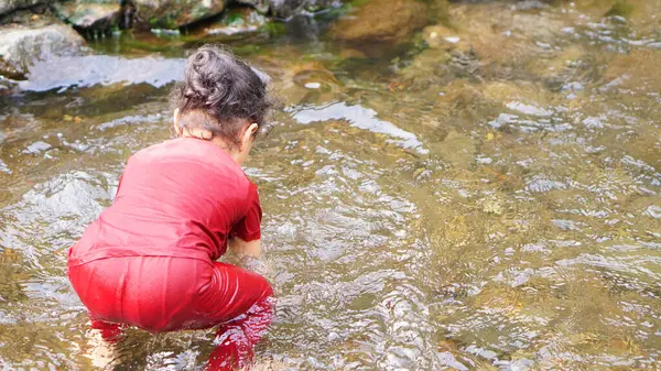 Kırmızı elbiseli bir kız çocuğu nehirde oynuyor.