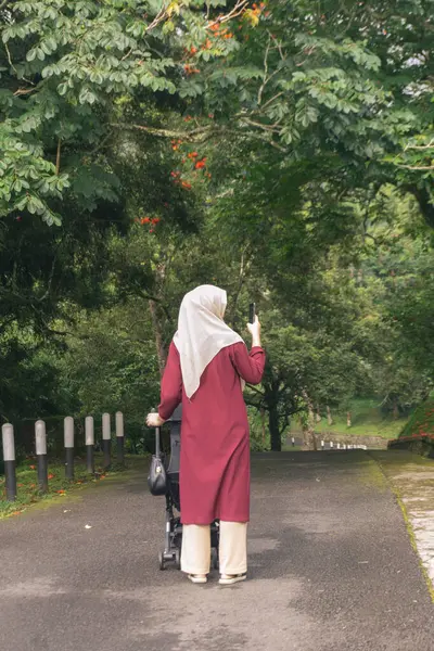 Jilbab annesi çocuğuyla parkta tek başına yürüyor.