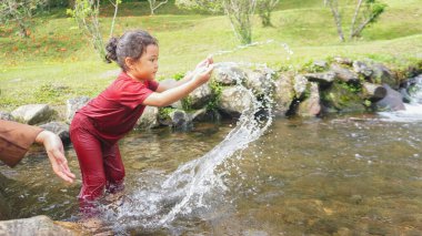 Annesiyle birlikte kırmızı elbiseli bir nehirde oynayan bir kız.