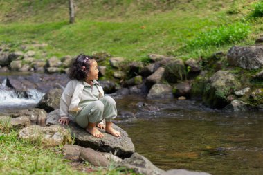 Kıvırcık saçlı bir kız, gülen yüzlü bir nehirde tatil yapar.
