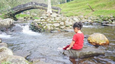 Kırmızı elbiseli bir kız çocuğu nehirde oynuyor.