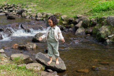 Kıvırcık saçlı bir kız, gülen yüzlü bir nehirde tatil yapar.