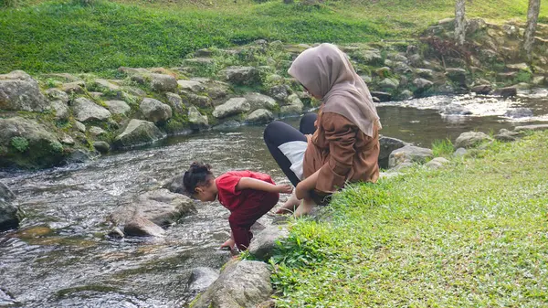 Başörtüsü Anne ve kızı nehirde birlikte oynuyorlar ve el ele tutuşuyorlar.
