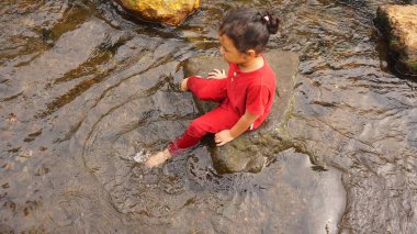 Kırmızı elbiseli bir kız çocuğu nehirde oynuyor.