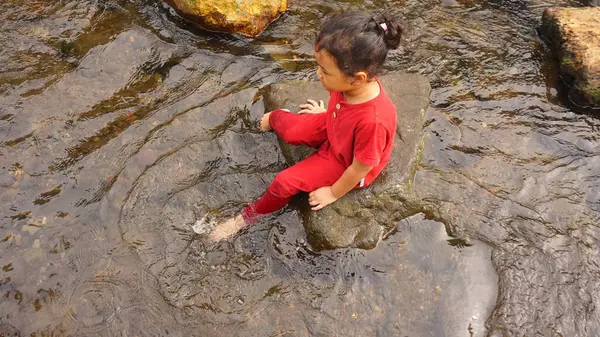 Kırmızı elbiseli bir kız çocuğu nehirde oynuyor.