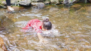 Kırmızı elbiseli bir kız çocuğu nehirde oynuyor.