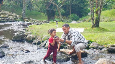 Baba ve kızı nehirde el ele oynuyorlar.