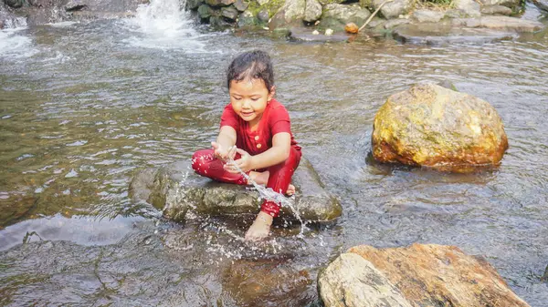 Kırmızı elbiseli bir kız çocuğu nehirde oynuyor.