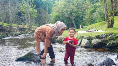 Anne ve kızı nehirde taş oynuyorlar.