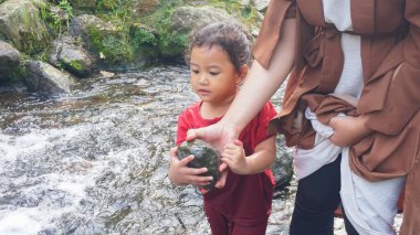 Anne ve kızı nehirde taş oynuyorlar.