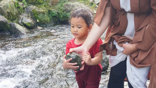 Anne ve kızı nehirde taş oynuyorlar.