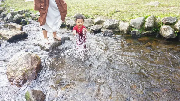 Annesiyle birlikte kırmızı elbiseli bir nehirde oynayan bir kız.