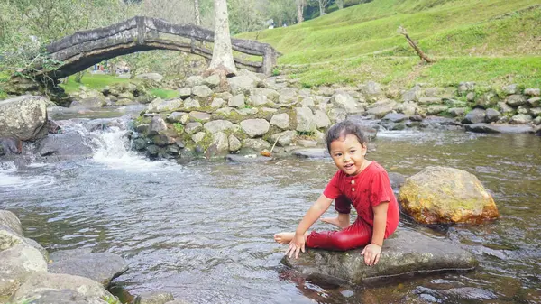 Kırmızı elbiseli bir kız çocuğu nehirde oynuyor.