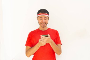 Endonezyalı genç adam, izole edilmiş beyaz saç bandıyla cep telefonu tutarken heyecanlandı.