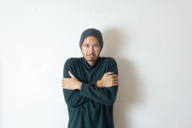 Kış giysileri giyen Endonezyalı adam kollarını kavuşturuyor.