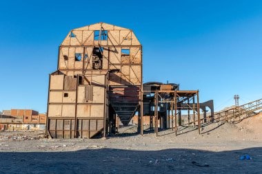 Old ruined coal preparation plant or coal handling in Kenadsa town, Bechar city, Algeria. Metallic structure remaining in a clear blue sky in background and dirt sandstones reg in foreground.