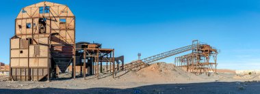 Old ruined coal preparation plant or coal handling in Kenadsa town, Bechar city, Algeria. Metallic structure remaining in a clear blue sky in background and dirt sandstones reg in foreground.