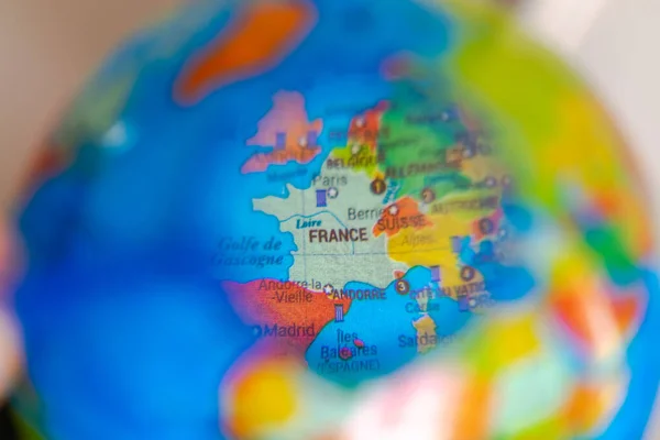 Globe with the world map of France seen under a magnifying glass. Close up macrophotograph with selective focus and shallow depth of field, the rest of the world is blurred. French language names.