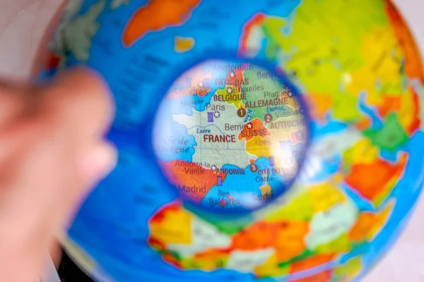 Globe with the world map of France seen under a hand hold magnifying glass. Close up macrophotograph with selective focus and shallow depth of field, the rest of the world is blurred. French language names.