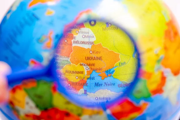 Globe with the world map of Ukraine seen under a magnifying glass. Close up macrophotograph with selective focus and shallow depth of field, the rest of the world is blurred. French language country names.