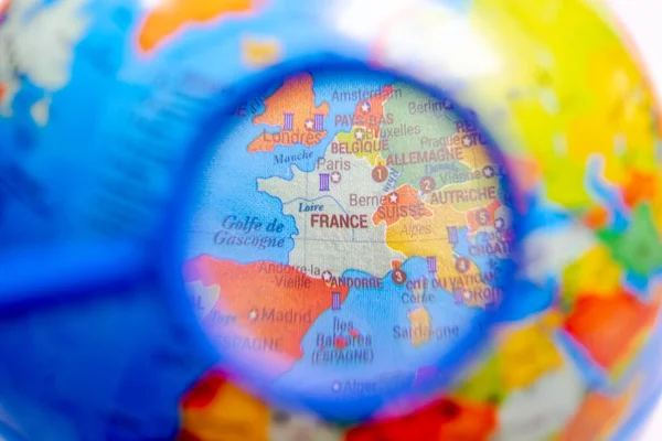 Globe with the world map of France seen under a magnifying glass. Close up macrophotograph with selective focus and shallow depth of field, the rest of the world is blurred. French language names.