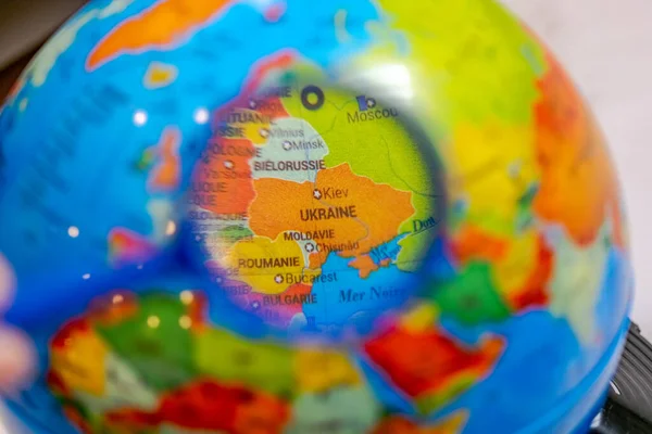 Globe with the world map of Ukraine seen under a magnifying glass. Close up macrophotograph with selective focus and shallow depth of field, the rest of the world is blurred. French language country names.