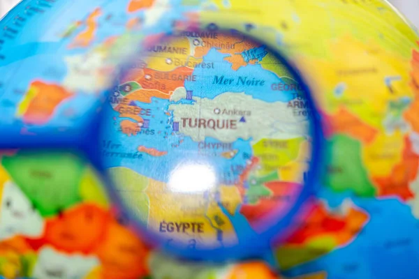 Globe with the world map of Turkey seen under a magnifying glass. Close up macrophotograph with selective focus and shallow depth of field, the rest of the world is blurred. French language country names.