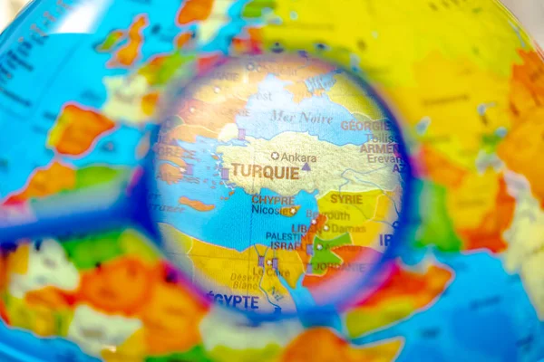 Globe with the world map of Turkey seen under a magnifying glass. Close up macrophotograph with selective focus and shallow depth of field, the rest of the world is blurred. French language country names.