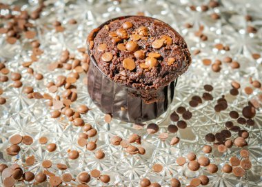 Dağınık çikolata parçalı ev yapımı kek, yakın çekim makrofotoğrafçılık, yandan parlayan beyaz güneş ışığı. Dar alan derinliği ile seçici odak, vignette ile bulanık arkaplan.