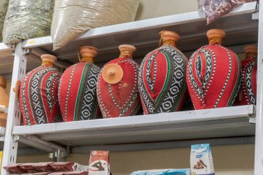 Cezayir - 29 Aralık 2022: El yapımı kil su sürahileri dokuma kumaş, Hint kostümleri ve aromatik baharatlar ve kurutulmuş bitkilerle dolu büyük çuvallar içeren pazar rafları.
