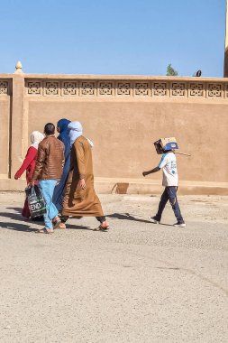Tamanrasset, Cezayir 2 Mart 2025 'te tanınmayan bir grup insan sokakta yürüyordu ve bir çocuk yüzünü örtmek ve kendini güneşten korumak için kafasına karton bir kutu takmıştı..