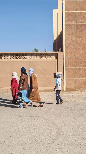 Tamanrasset, Cezayir 2 Mart 2025 'te tanınmayan bir grup insan sokakta yürüyordu ve bir çocuk yüzünü örtmek ve kendini güneşten korumak için kafasına karton bir kutu takmıştı..