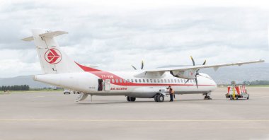 Cezayir - 9 Nisan 2024 Cezayir Havayolları ATR 72-800 uçağı, uçakları dışarıdan kontrol eden bir işçiyle birlikte, geniş, boş bir pistte park halinde. Uzakta bir dağ zinciri ve bulutlu bir gökyüzü