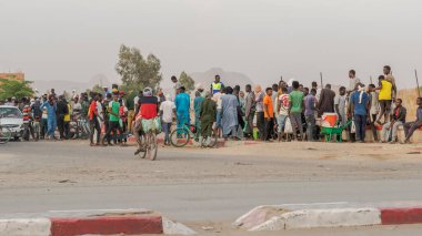 Tamanrasset, Cezayir - 22 Mart 2025: Siyah Afrikalılardan oluşan bir kalabalık kaldırımda toplandı, yaya ve bisikletlerle, yol kenarında birbirleriyle sohbet ediyorlardı..