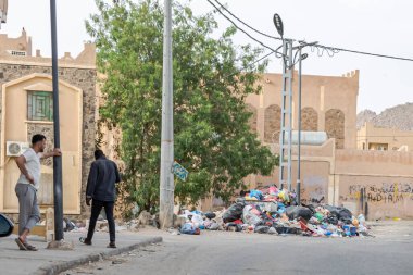 Tamanrasset, Cezayir 22 Mart 2025: Çöp yığını Arapçadaki el yazısıyla yazılmış ahşap bir tabelanın yanına dökülüyor ve 