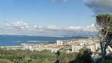 Cezayir 'in panoramik manzarası yükseldi: Hamma' nın botanik bahçesi, elektrik santrali, sahil binaları, gemileri ve Sablettes park marinası ile deniz ve bulutlu mavi gökyüzünün altındaki Cezayir Büyük Camii..