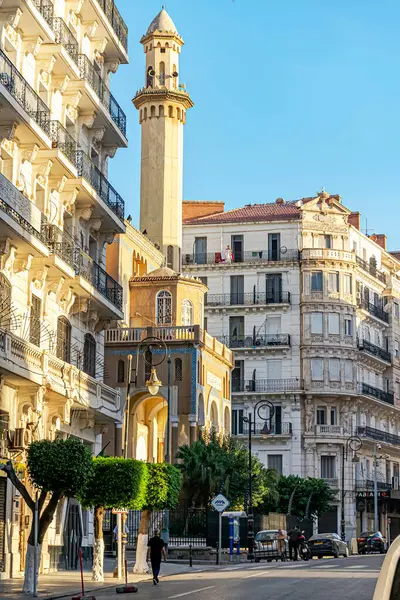 Cezayir, Cezayir - 28 Ekim 2022: Cezayir 'in Abane Ramdane sokağındaki İbn Badis camiinin yan görüntüsü. Arabalar park edilmiş ve insanlar yürüyor. Binalarda parlayan ağaçlar ve güneş ışığı.