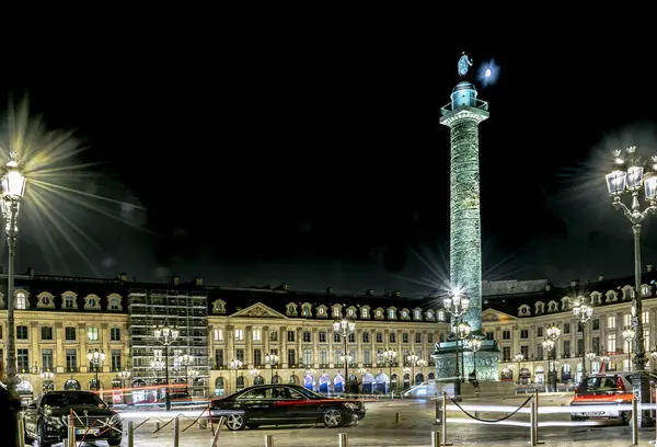 Place Vendme, Paris, Fransa - 19 Ekim 2018: yeşilimsi ışıkla aydınlatılmış sütun, klasik binalar, dekoratif cepheler, parlayan sokak lambaları ve karanlık bir gökyüzünün altında gece yarısı park edilmiş arabalar ile çevrili.