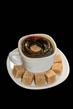 Bir fincan sade kahve ve bir şeker yüzeye dökülerek bir sıçramaya neden olur, bir fincan dolusu siyah arkaplanda izole edilmiş kahverengi şeker dolu beyaz bir fincan içinde servis edilir..