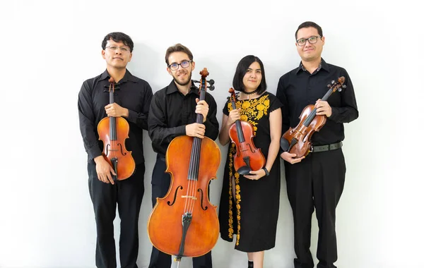 multiethnic group of musicians, string quartet posing for camera not playing. three men and a girl mixed group of musicians with wooden string instruments, standing against a white wall
