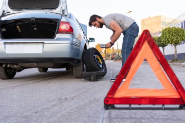 worried man changing a flat tire, car with opened trunk taking spare tire